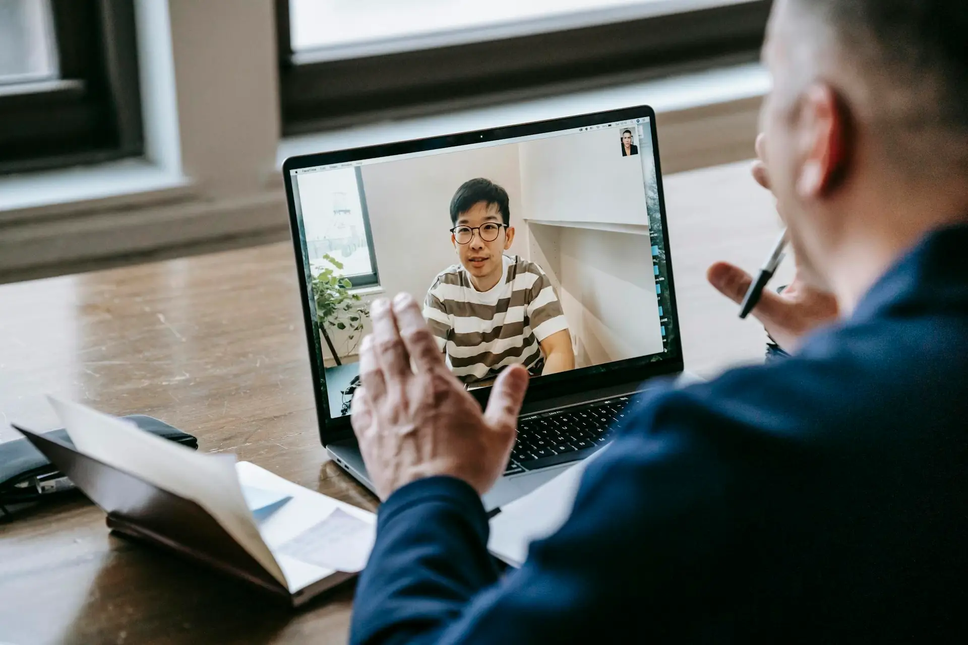 Two professionals engaged in an online video conference on a laptop in an indoor setting.